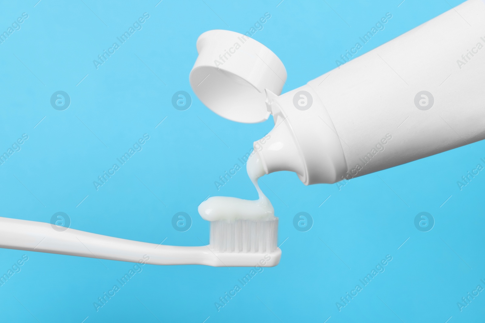 Photo of Applying paste on toothbrush against light blue background, closeup