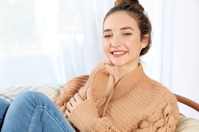 Photo of Beautiful teenage girl in warm cozy sweater sitting near window at home