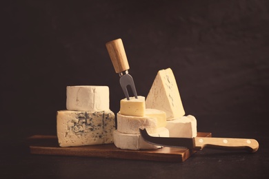 Different types of cheese, knife and fork on black table