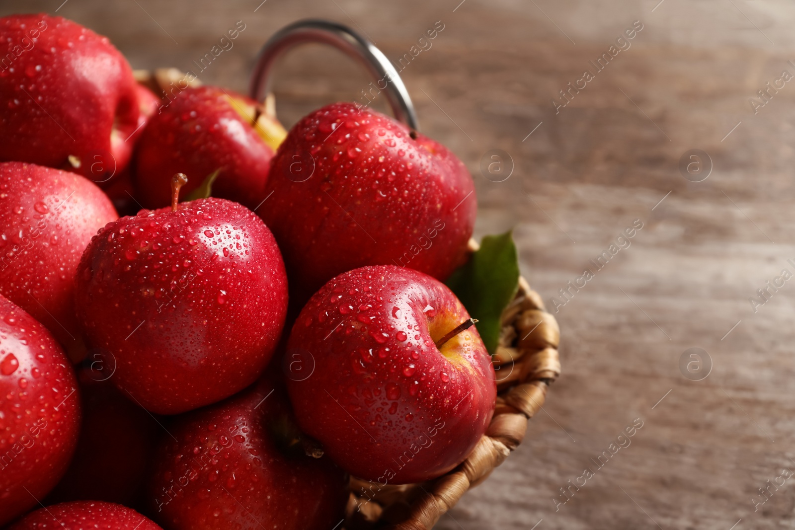 Photo of Basket with fresh ripe red apples on wooden table, closeup