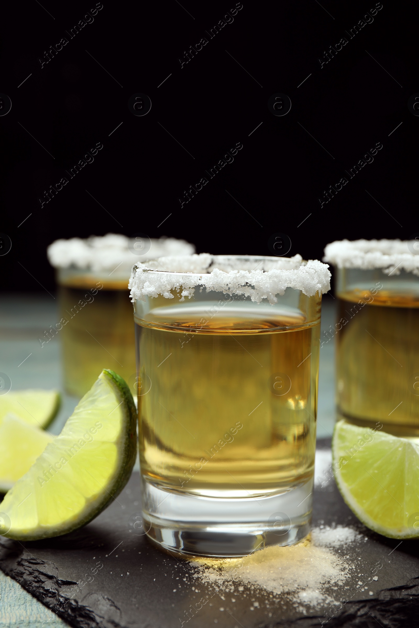 Photo of Mexican Tequila shots, lime slices and salt on blue wooden table