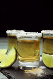 Photo of Mexican Tequila shots, lime slices and salt on blue wooden table