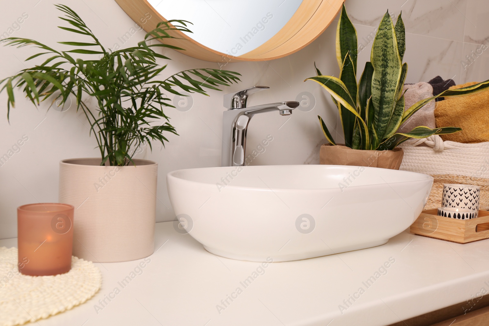 Photo of Bathroom counter with sink, candles and beautiful green houseplants near white marble wall