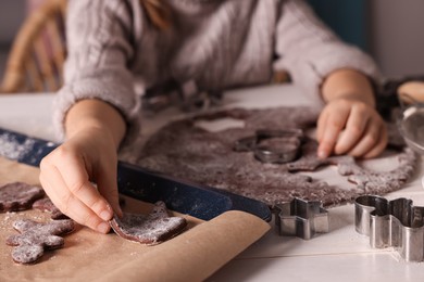 Photo of Little child making Christmas cookies at white wooden table, closeup