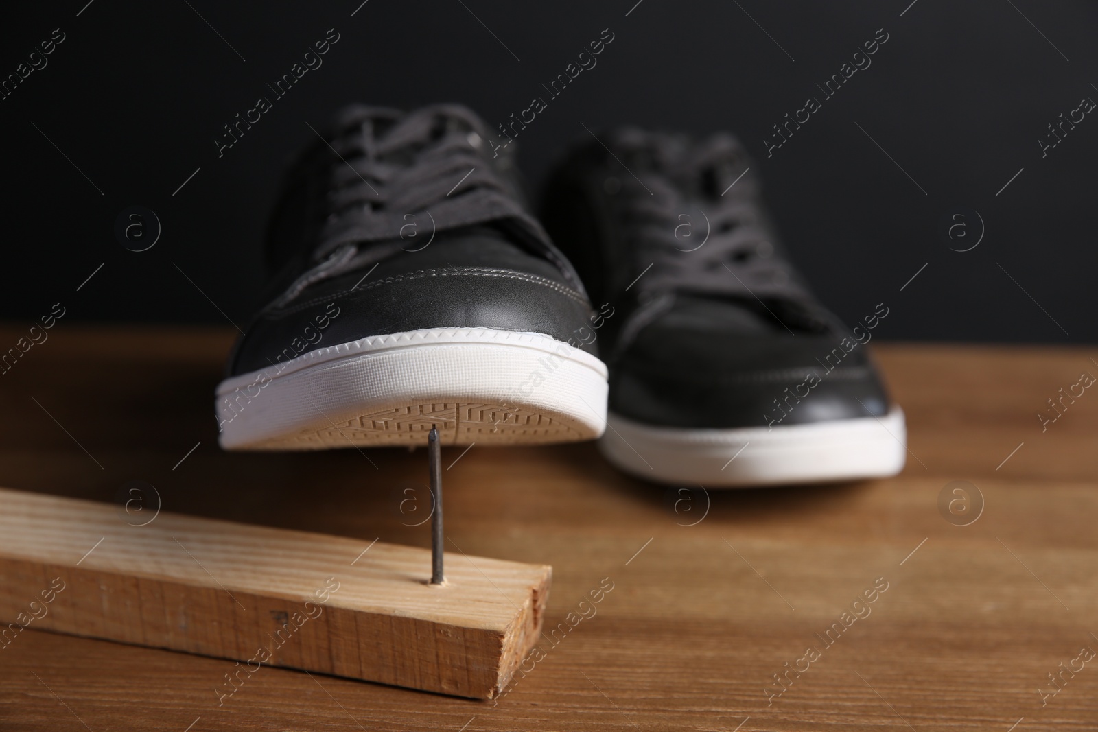 Photo of Metal nail in wooden plank and shoes on table