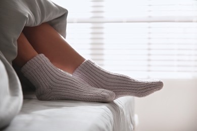 Photo of Woman wearing knitted socks under blanket in bed, closeup
