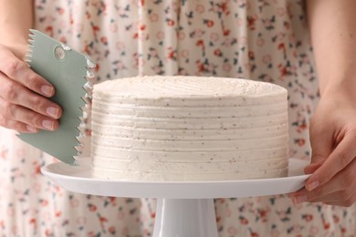 Woman using scraper to decorate cake, closeup