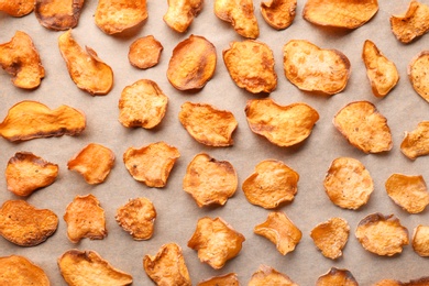 Photo of Sweet potato chips on parchment, flat lay