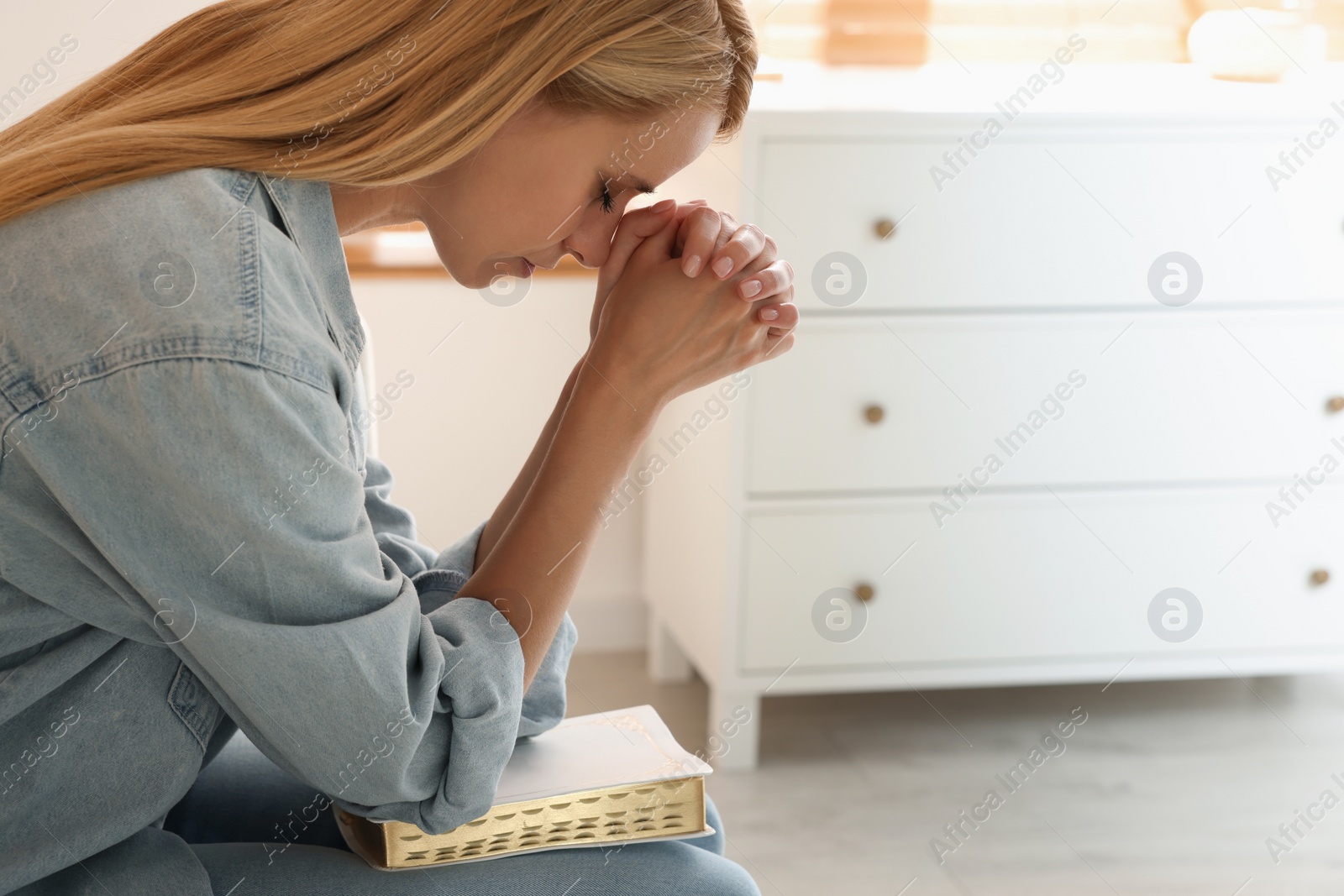 Photo of Religious young woman with Bible praying indoors. Space for text