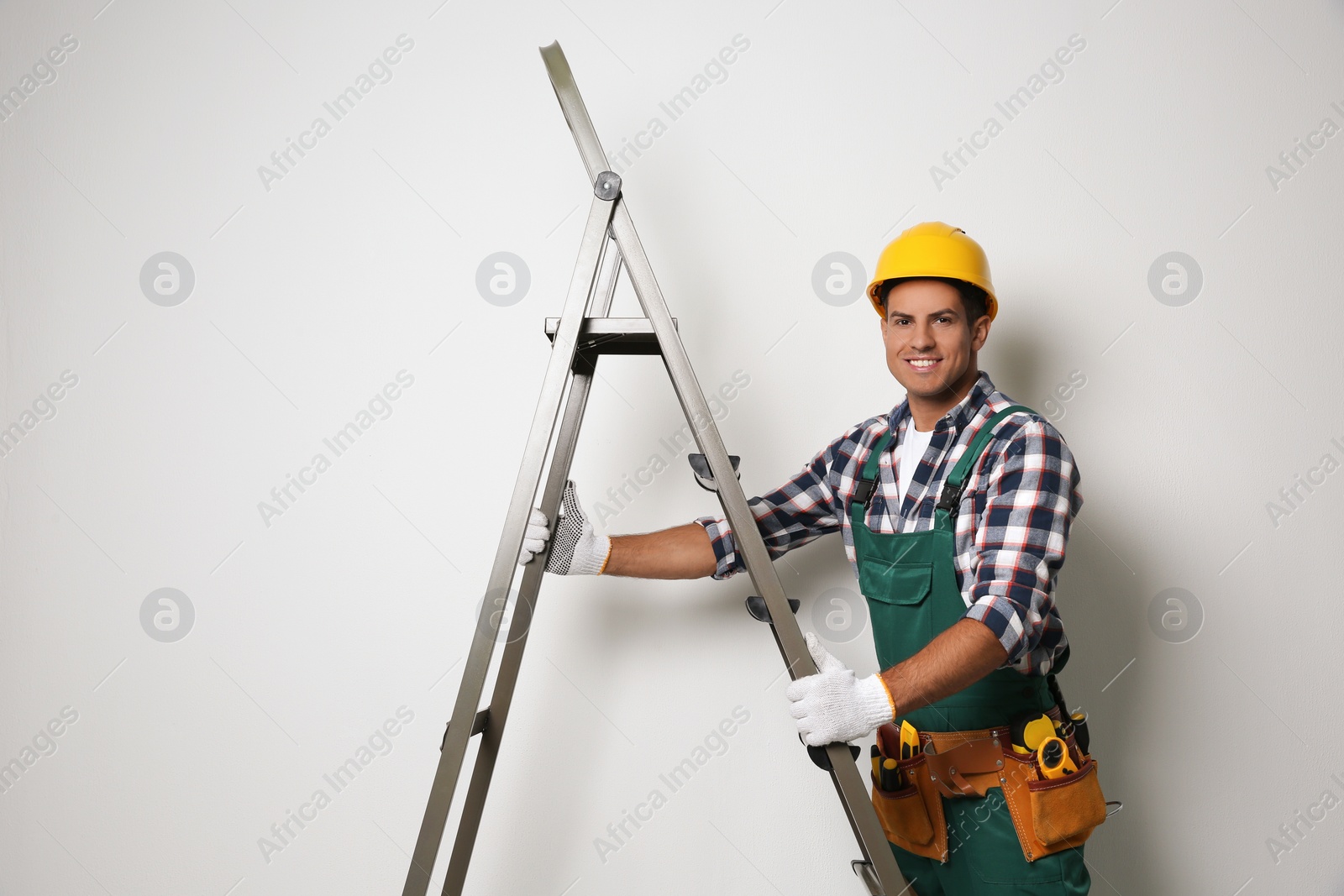 Photo of Professional builder with metal ladder on light background