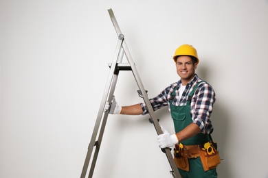 Photo of Professional builder with metal ladder on light background