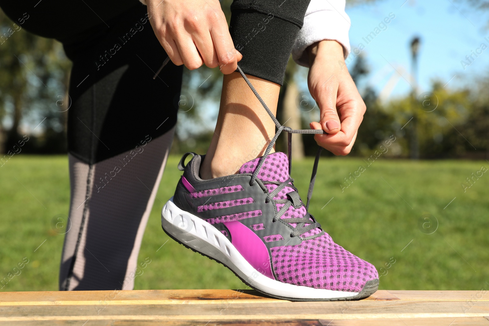 Image of Sporty woman tying shoelaces in park on sunny morning, closeup