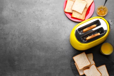 Photo of Yellow toaster with roasted bread, glass of juice and jam on grey table, flat lay. Space for text
