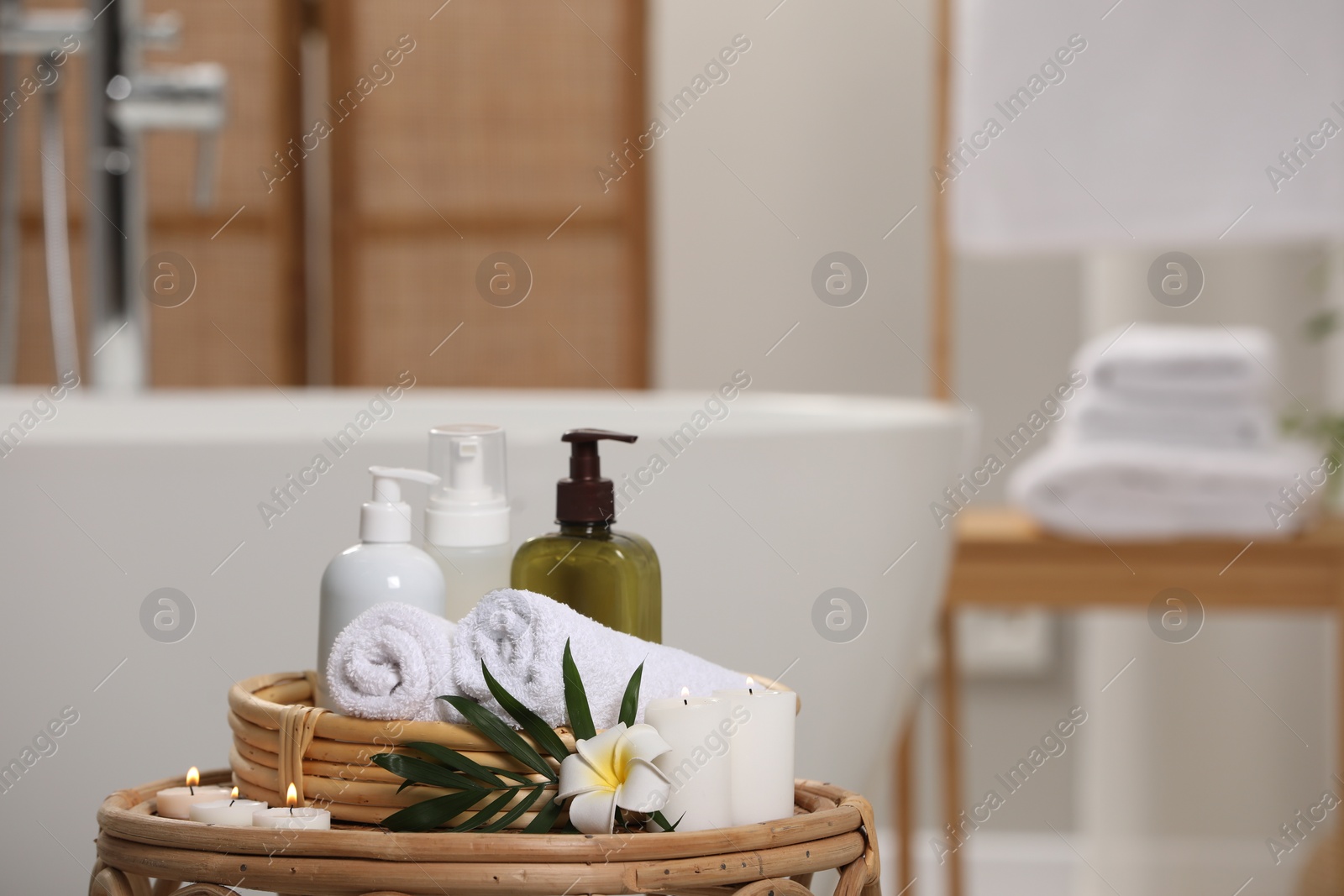 Photo of Spa products, burning candles, plumeria flower and tropical leaf on table in bathroom. Space for text