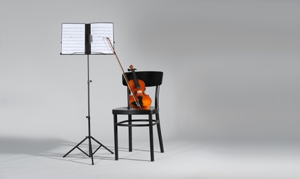 Photo of Violin, chair and note stand with music sheets on grey background. Space for text