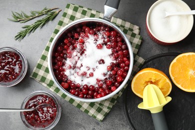 Making cranberry sauce. Fresh cranberries with sugar in saucepan and ingredients on gray table, flat lay