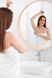 Beautiful young woman applying deodorant after shower in bathroom