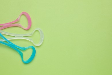 Colorful tongue cleaners on light green background, flat lay. Space for text