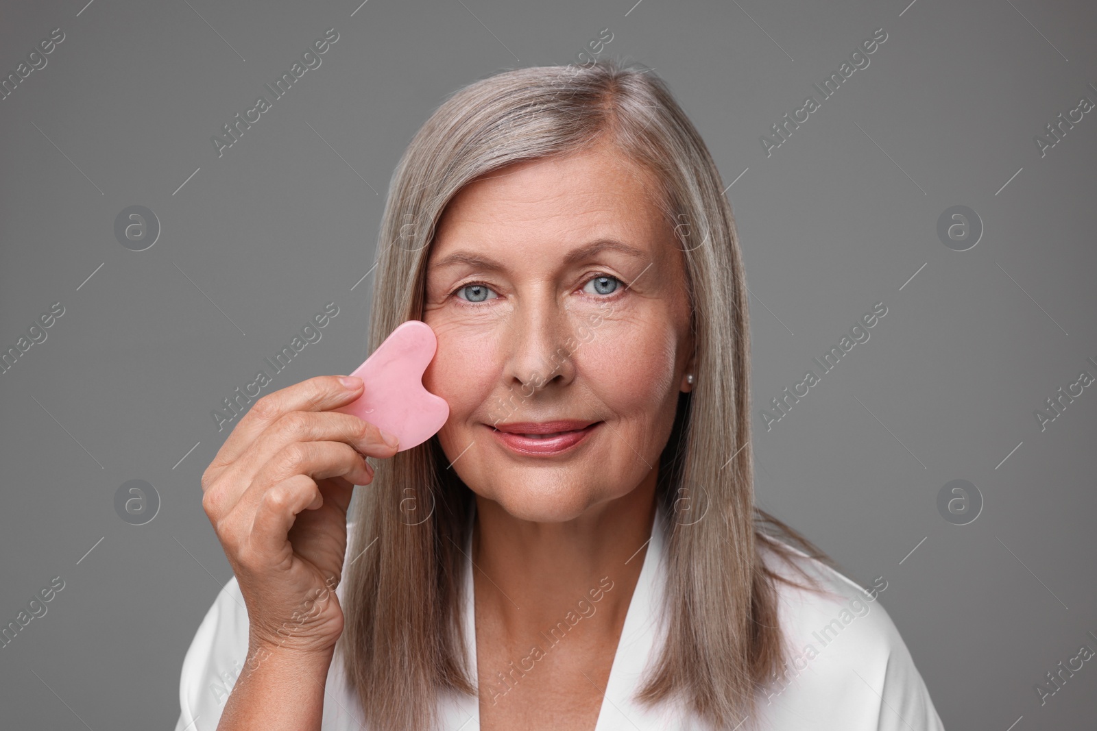 Photo of Woman massaging her face with rose quartz gua sha tool on grey background