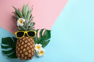 Photo of Top view of pineapple with sunglasses, tropical leaves and flowers on color background, space for text. Creative concept