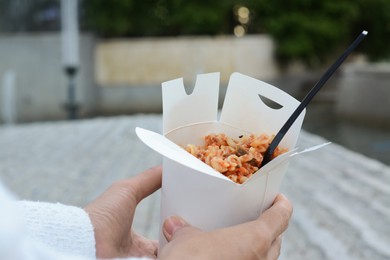 Woman holding paper box of takeaway noodles with fork outdoors, closeup. Street food