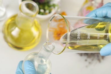 Scientist developing cosmetic oil at white table, closeup