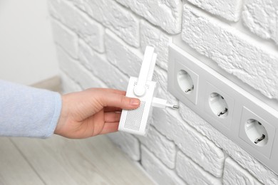 Woman inserting wireless Wi-Fi repeater into power socket indoors, closeup