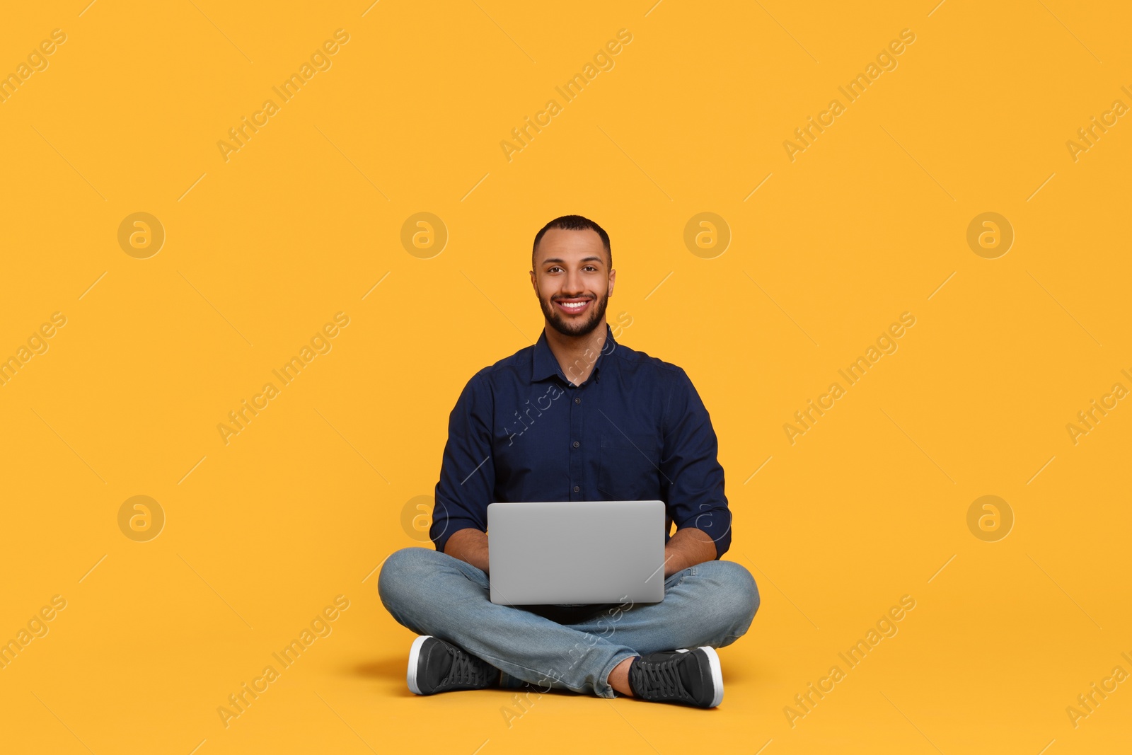 Photo of Smiling young man working with laptop on yellow background