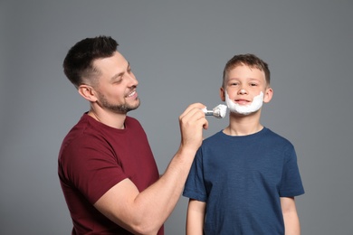 Dad applying shaving foam on son's face, grey background