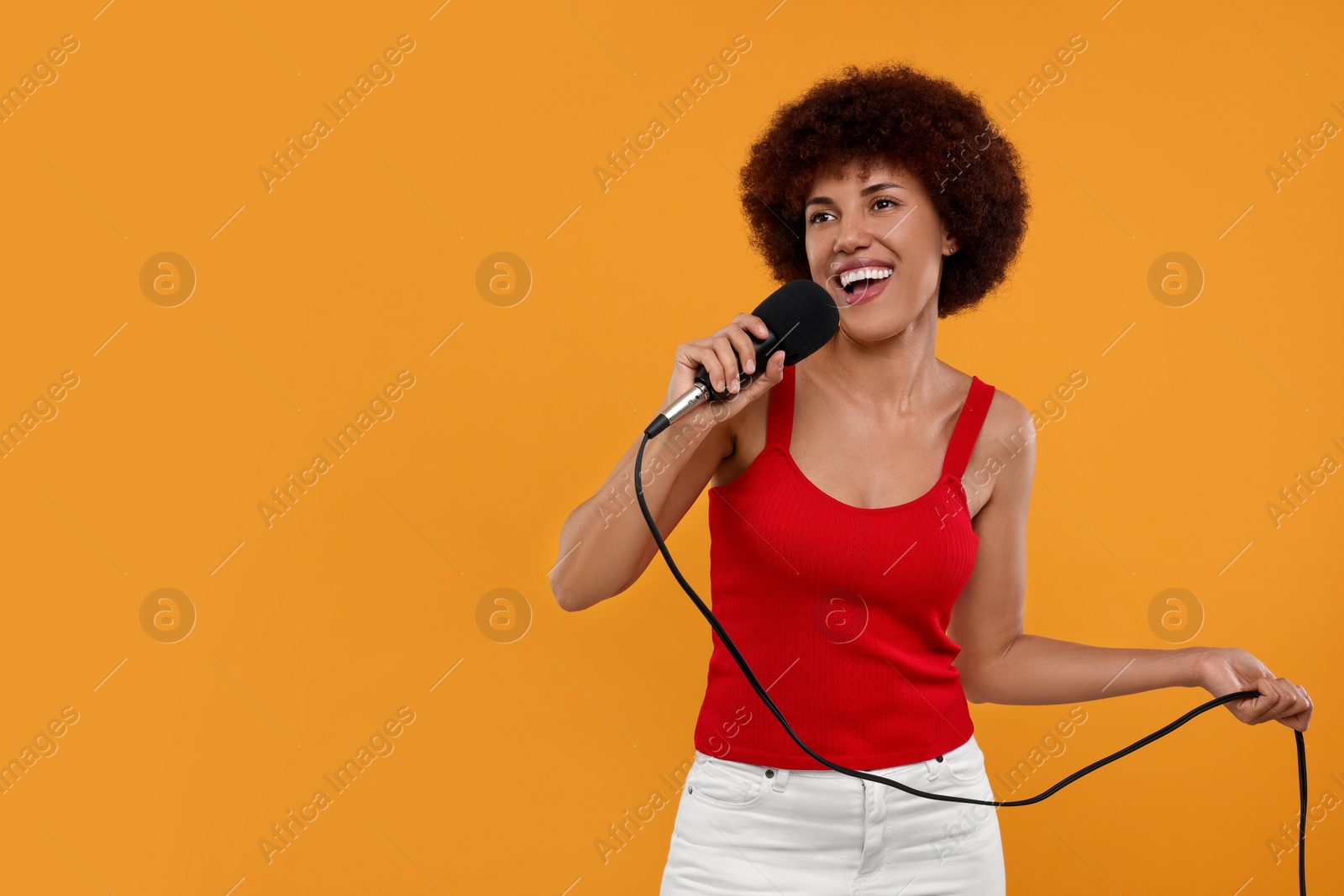 Photo of Curly young woman with microphone singing on yellow background, space for text