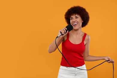 Curly young woman with microphone singing on yellow background, space for text