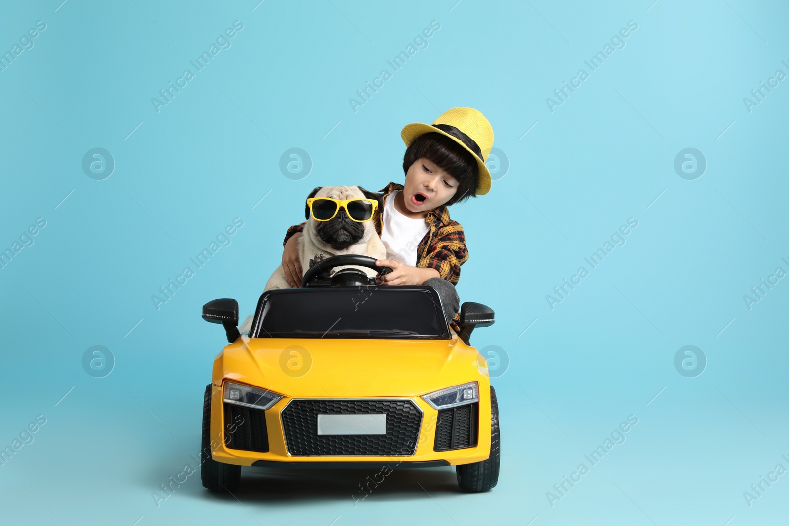 Photo of Little boy with his dog in toy car on light blue background