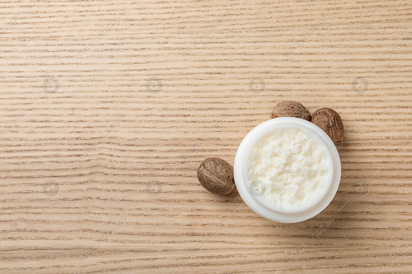 Photo of Jar of shea butter, nuts and space for text on wooden background, top view