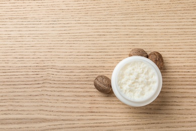 Jar of shea butter, nuts and space for text on wooden background, top view