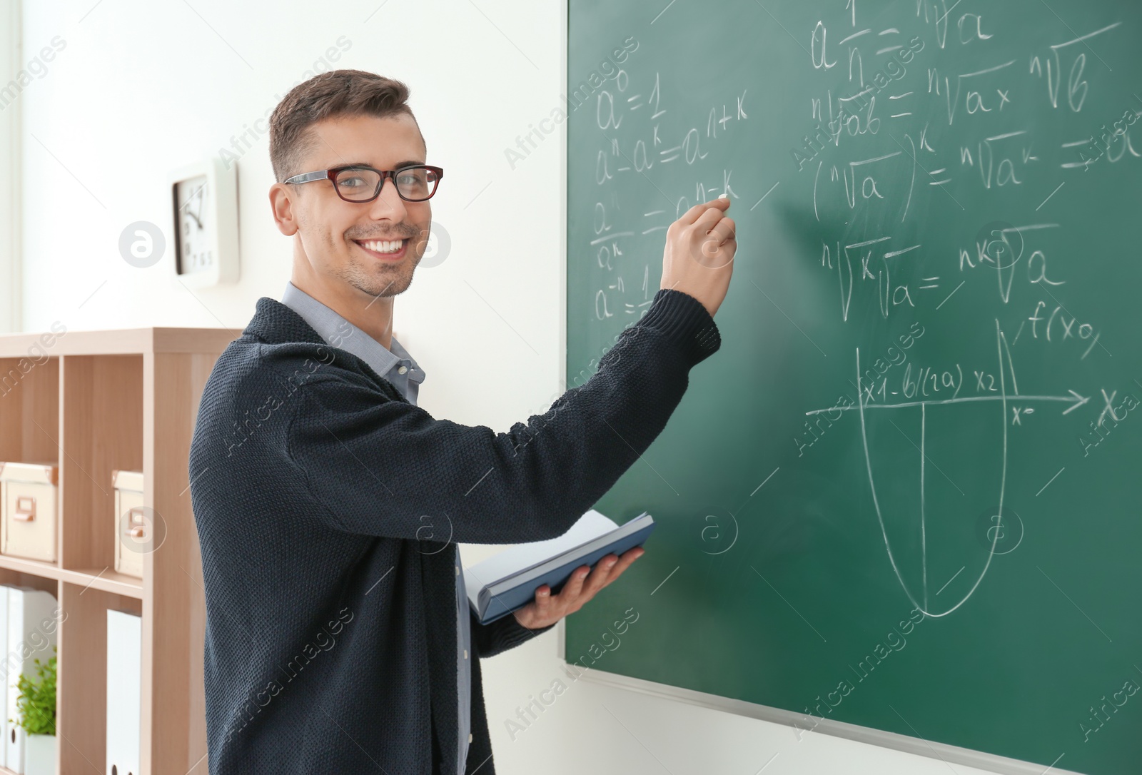 Photo of Young male teacher writing on blackboard in classroom