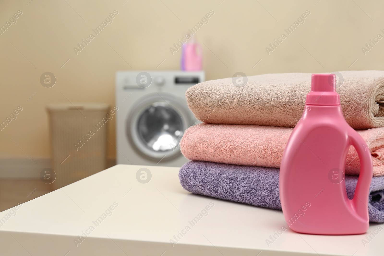 Photo of Clean towels and bottle of detergent on table in laundry room. Space for text