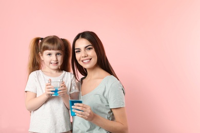 Photo of Little girl and her mother with mouthwash on color background, space for text. Teeth and oral care