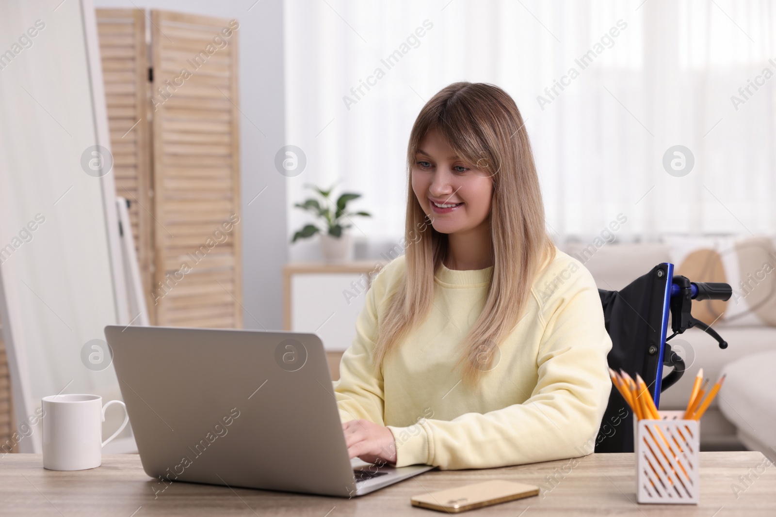 Photo of Woman in wheelchair using laptop at table in home office