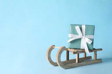 Photo of Wooden sleigh with Christmas gift box on light blue background, space for text