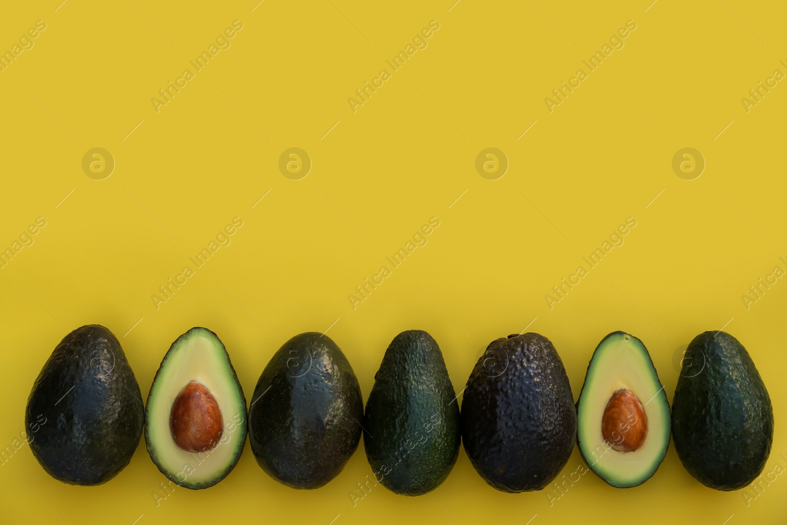 Photo of Fresh whole and cut avocados on yellow background, flat lay. Space for text