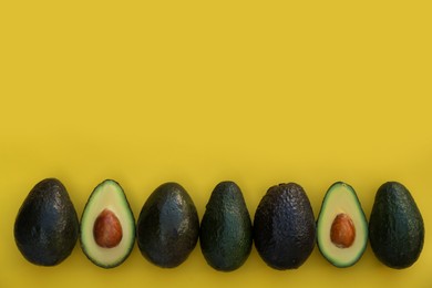 Photo of Fresh whole and cut avocados on yellow background, flat lay. Space for text
