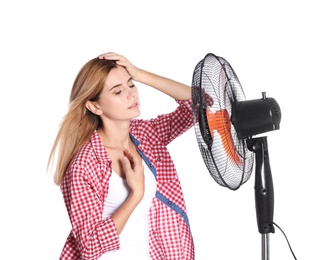 Woman suffering from heat in front of fan on white background