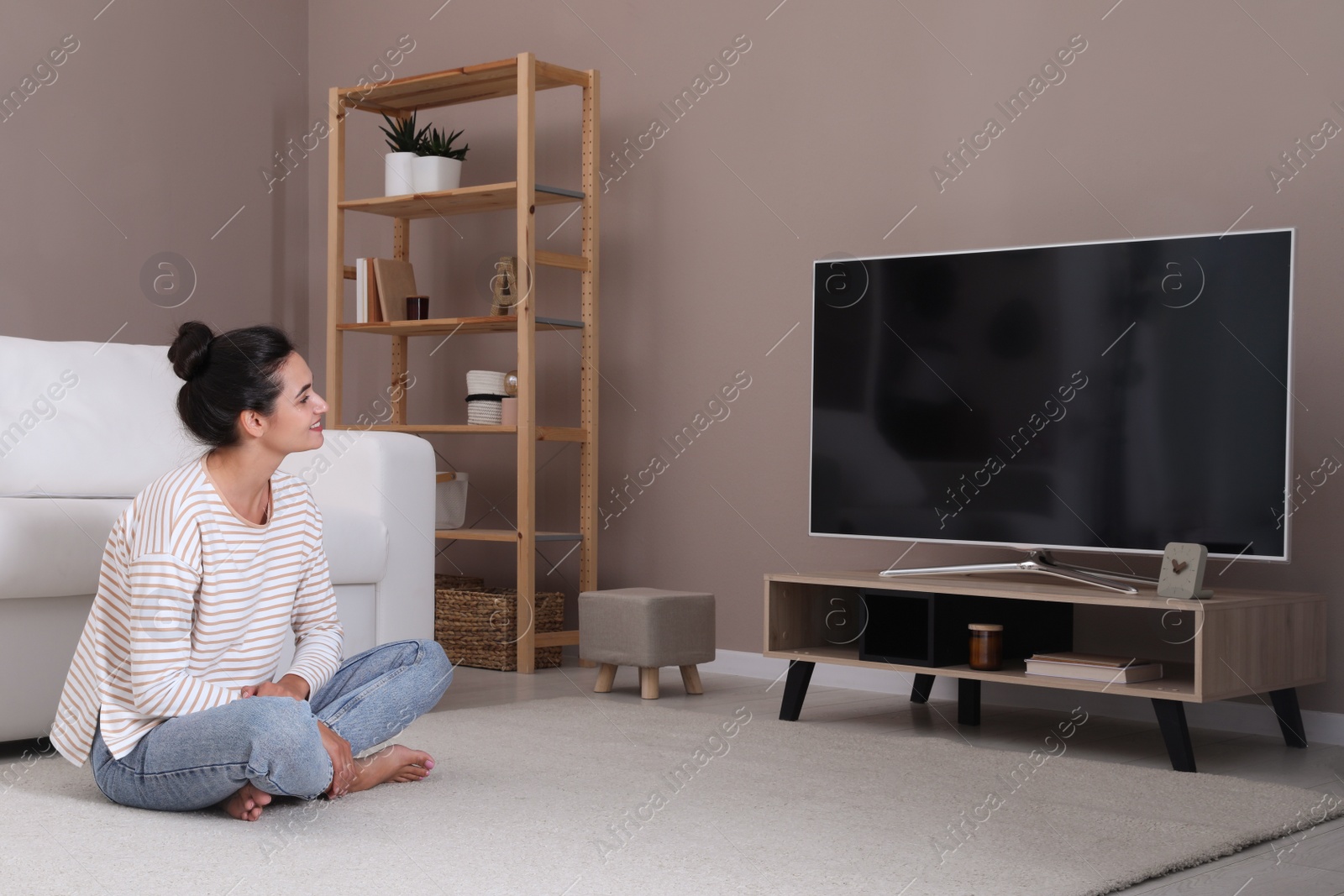 Photo of Woman watching television at home. Living room interior with TV on stand