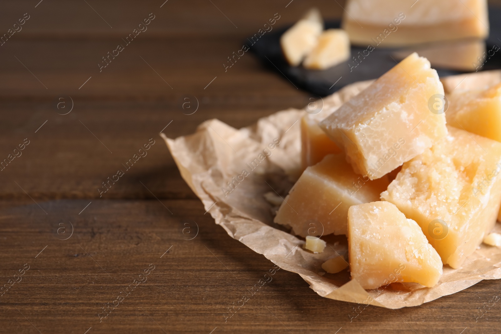 Photo of Pieces of delicious parmesan cheese on wooden table, closeup. Space for text