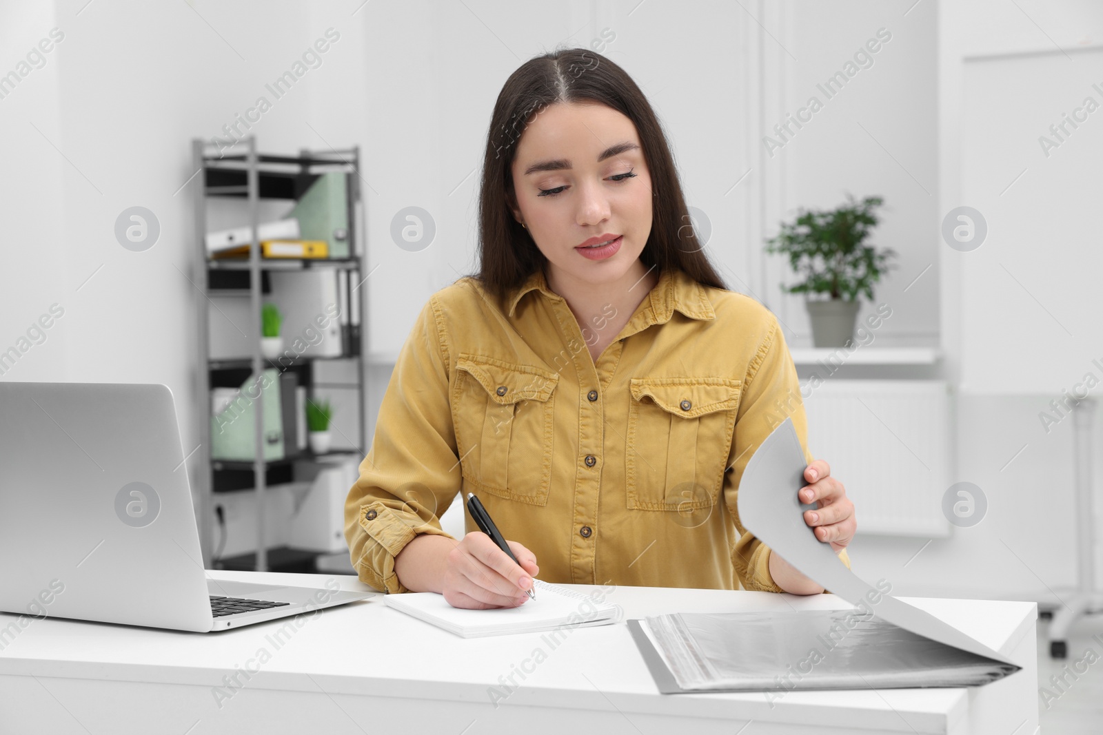 Photo of Young female intern working with laptop at table in office