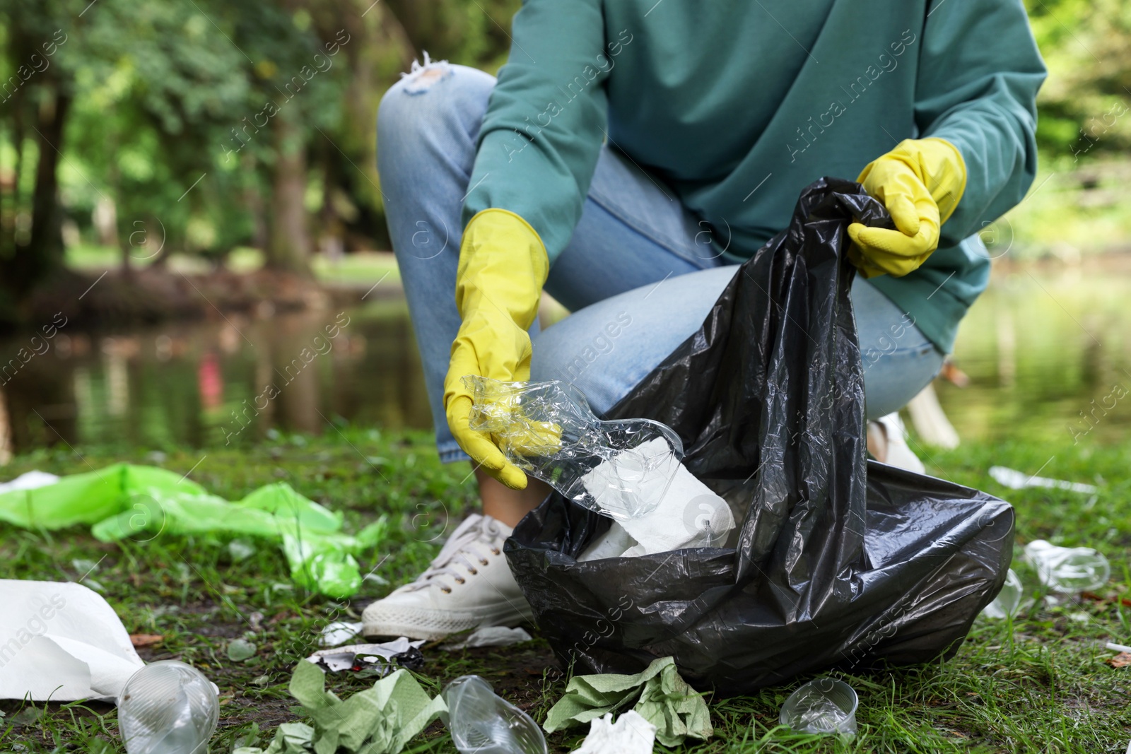 Photo of Woman with plastic bag collecting garbage in park, closeup