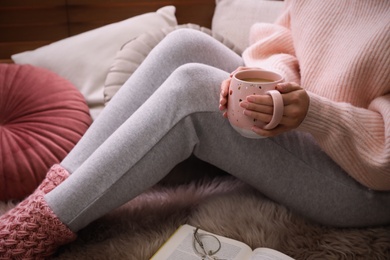 Woman with cup of hot drink resting at home, closeup