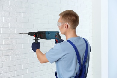 Photo of Handsome young working man using rotary hammer indoors. Home repair