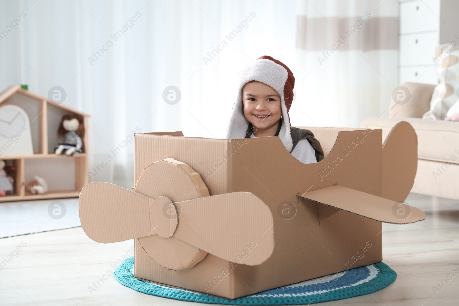 Photo of Cute little boy playing with cardboard airplane in living room