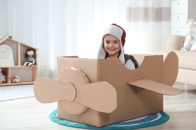Photo of Cute little boy playing with cardboard airplane in living room